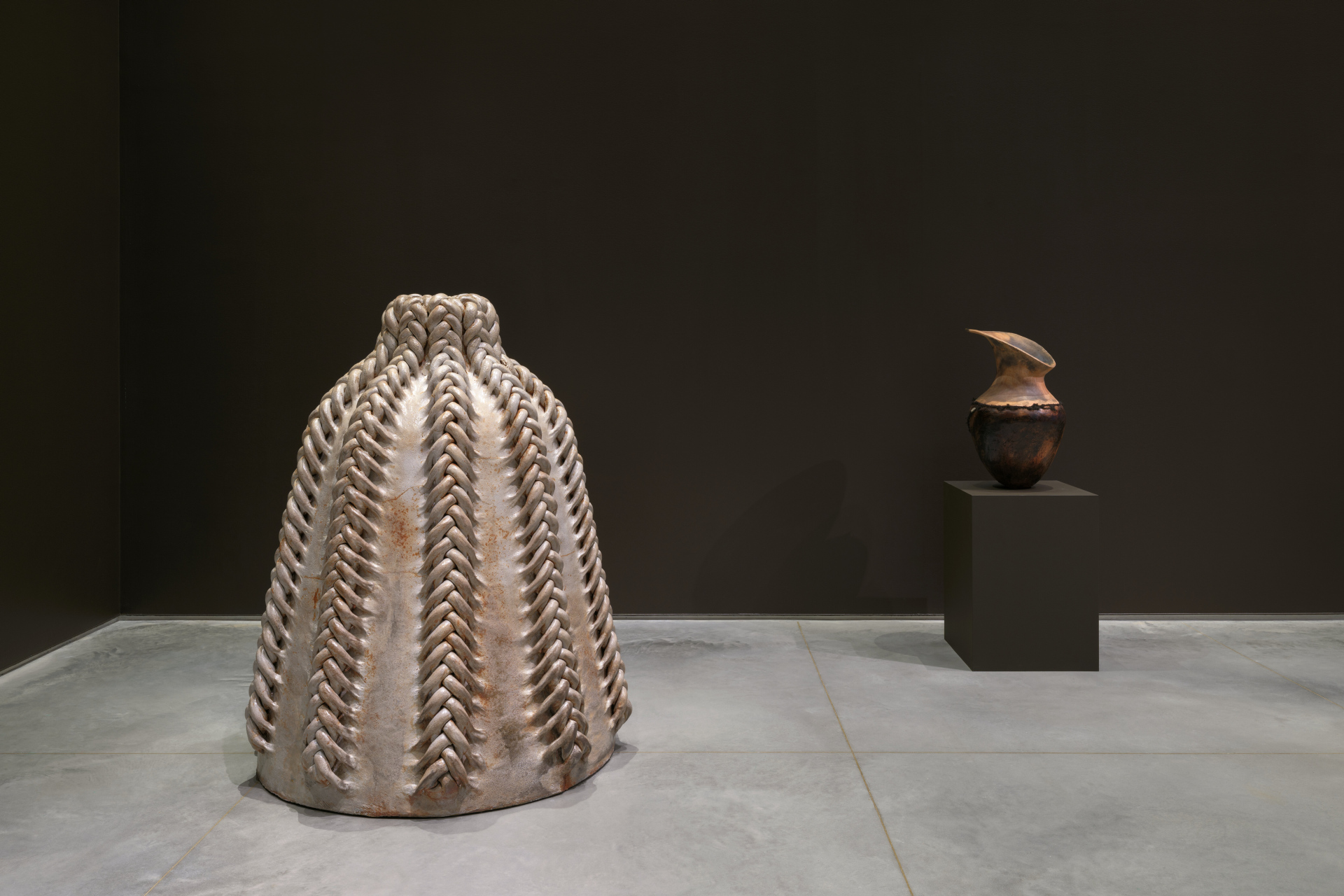 A five-feet tall, dome-like sculpture with braided accents. Next to a pit-fired ceramic pot.