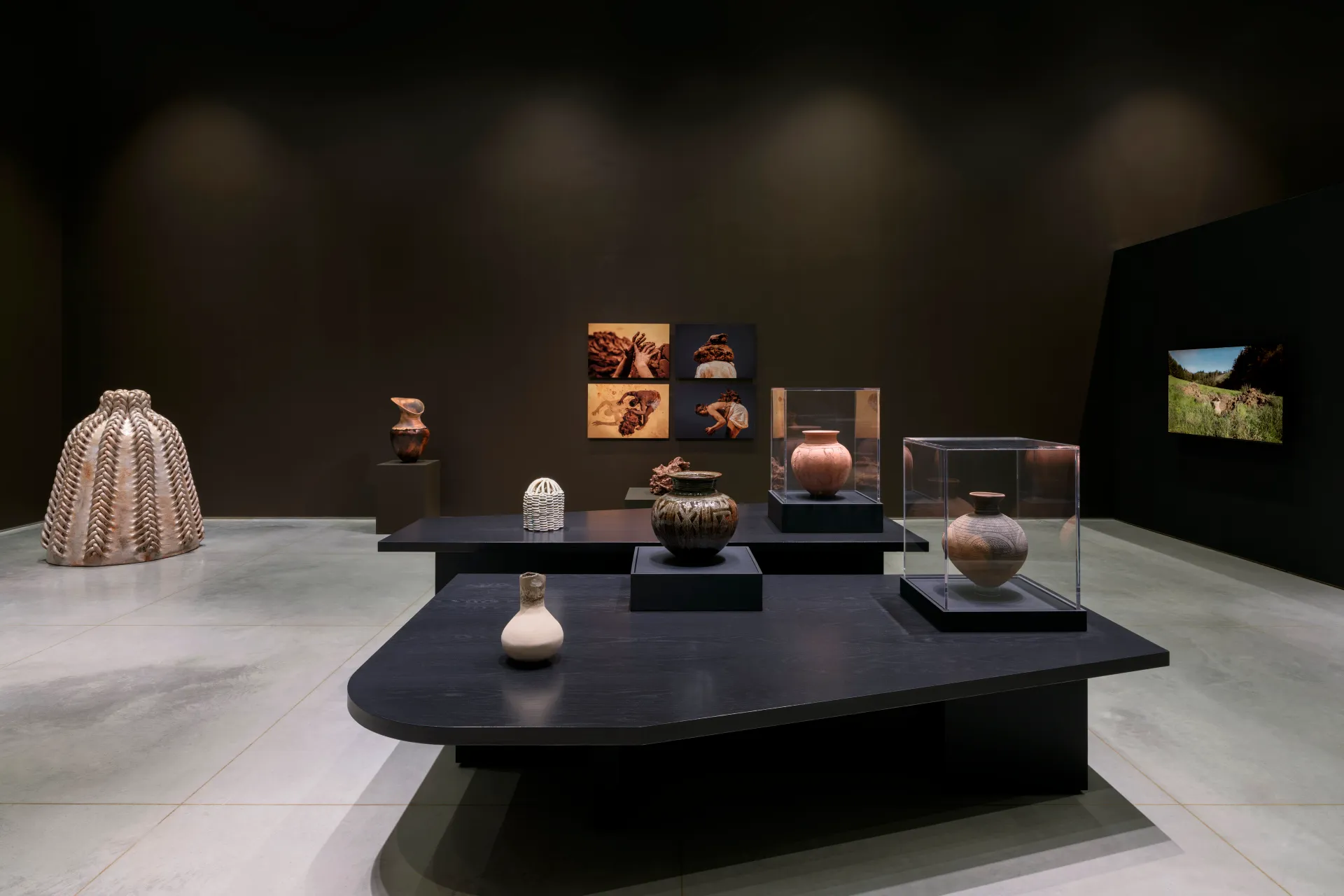 An side-installation view of a gallery exhibition with various clay sculptures and vases, video, and photography.