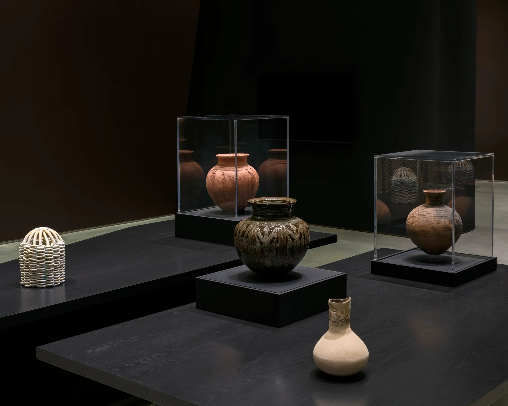 A gallery installation of five varied clay pots on a dimensional black table.