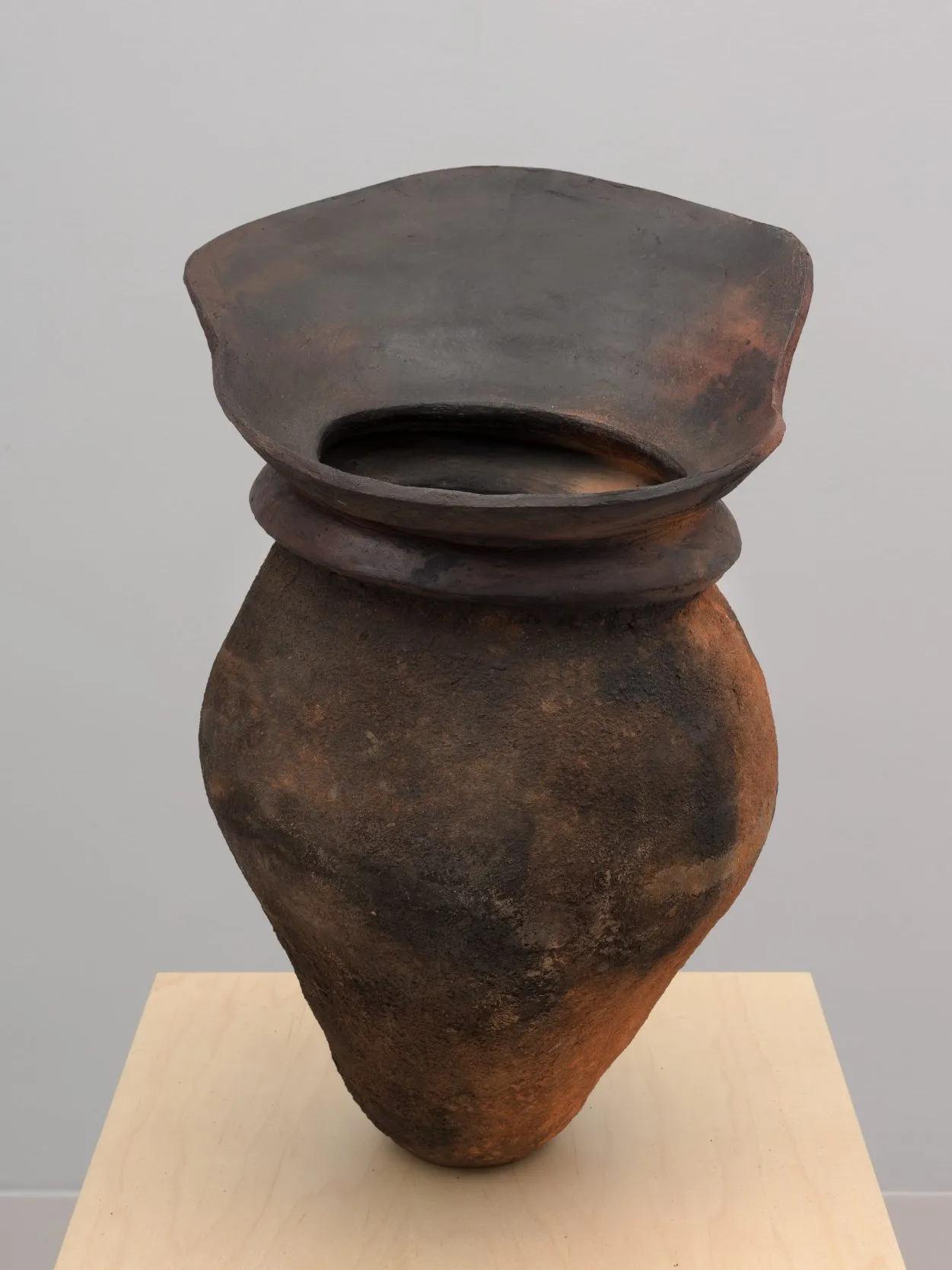 A ceramic vase with a heart-like shaped body that extends to a coiled neck and a tall, irregular mouth.