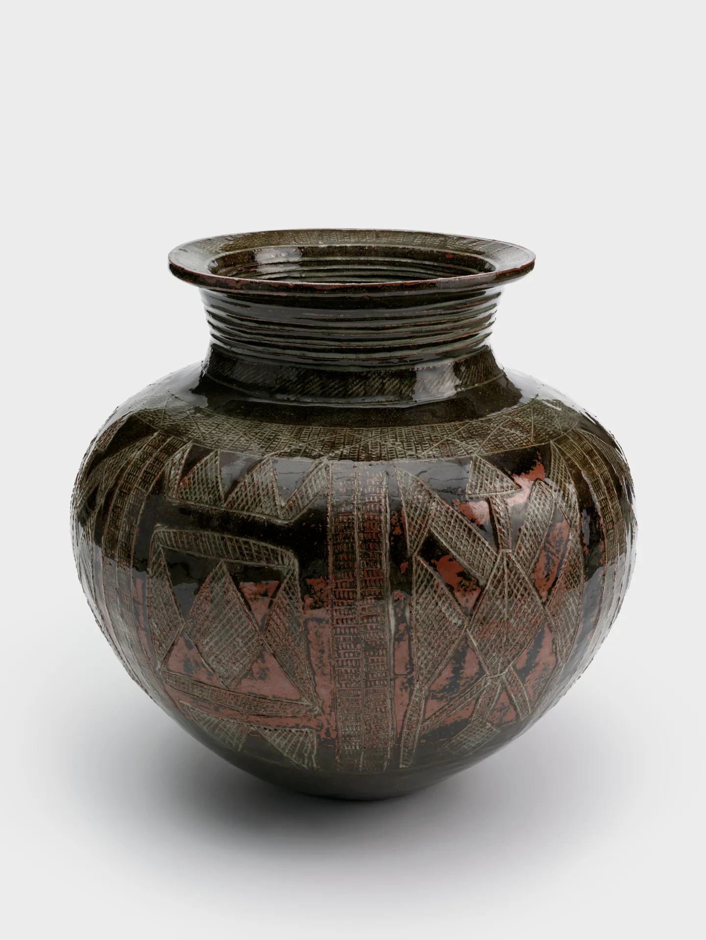 A glazed ceramic jar with a coiled neck and geometric designs made up of thin incised crosshatching throughout.