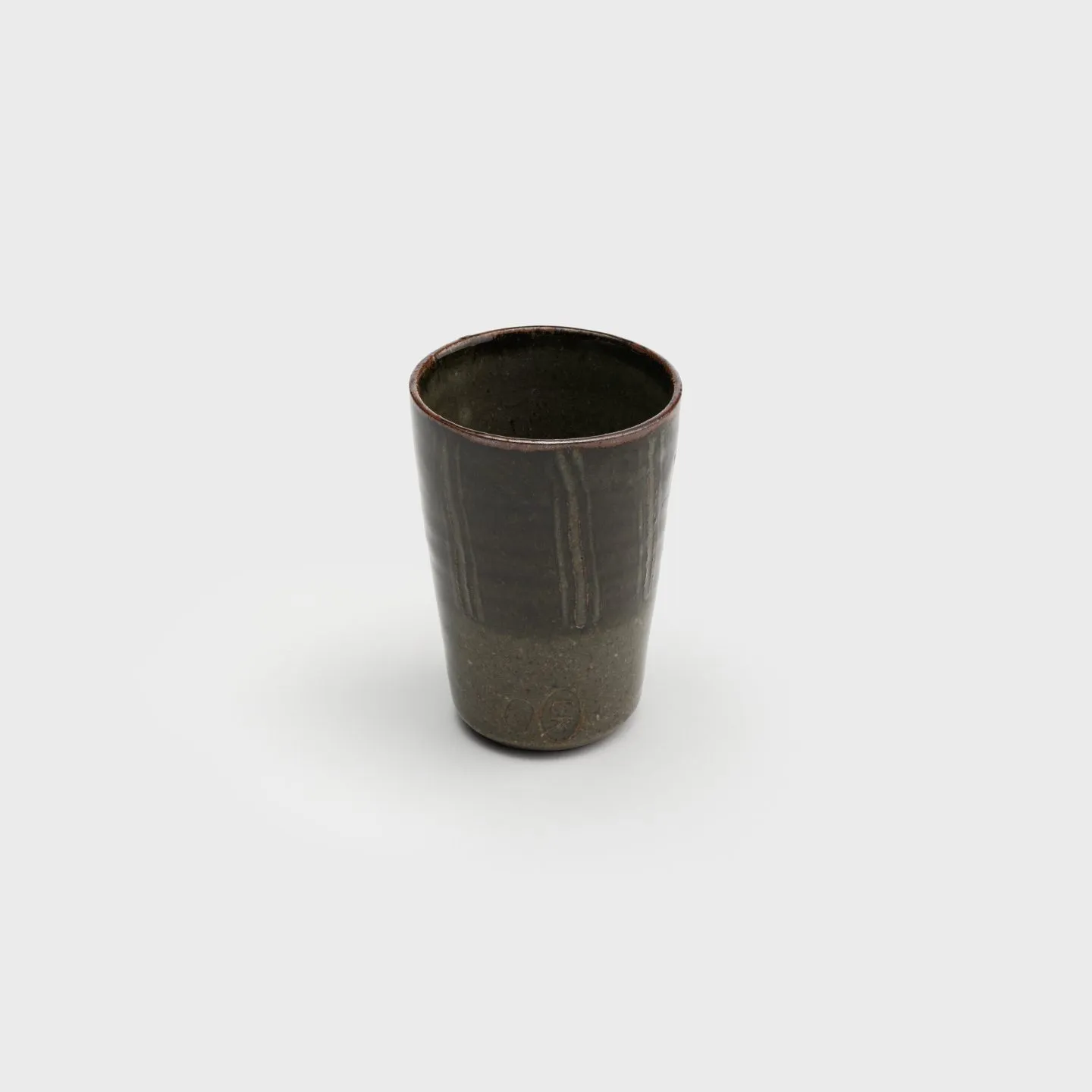 A ceramic cup with glossy earthtone glazes and a pattern of vertical stripes carved into the surface.