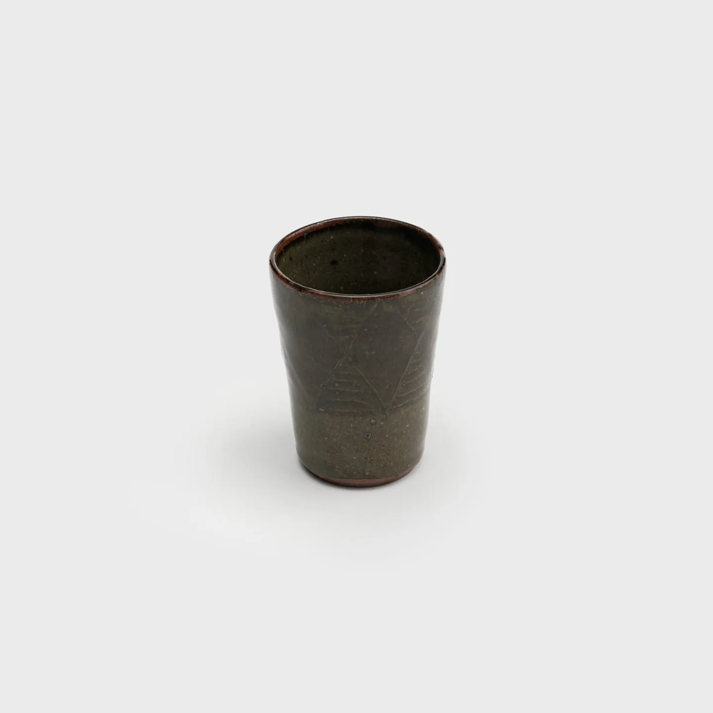A ceramic cup with glossy earthtone glazes and a pattern of diamonds and stripes carved into the surface.