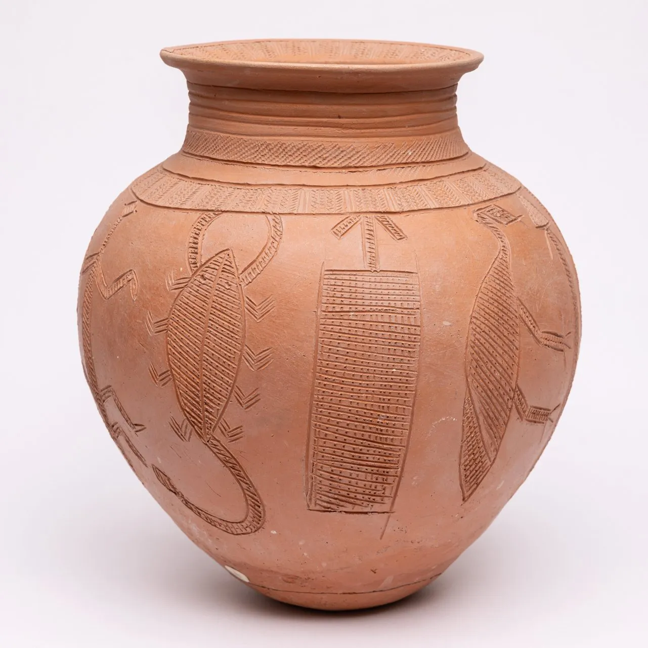 Unglazed ceramic pot with intricate line carvings of creatures, symbols, and patterns.