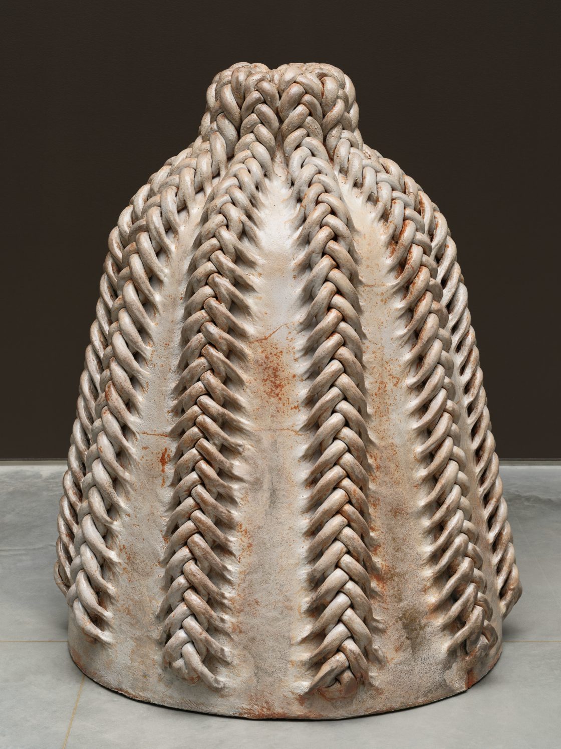 A large sculptural clay vessel that is barrel-shaped with braided accents down the seams.