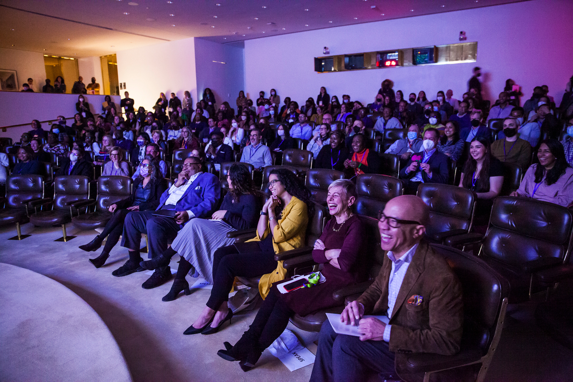 An audience in the Ford Foundation Center for Social Justice auditorium smiles and laughs during an event. The diverse crowd is seated in rows, with key figures in the foreground.