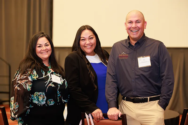 Three smiling Indigenous leaders (two women and one man) stand together at a conference. Keywords: Tribal Digital Sovereignty, Native American technology, digital equity, community leaders.
