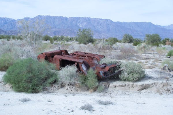 A corroded car abandoned and flipped upside down in a dessert.