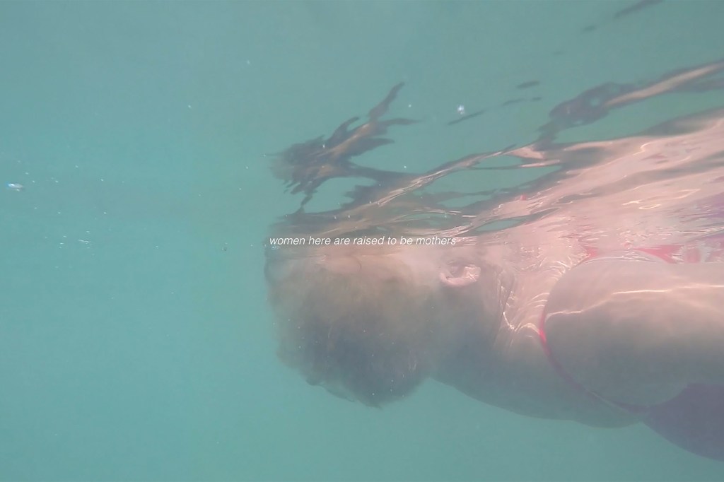 A photo of a short-haired older-woman swimming with white text overlaid "women here are raised to be mothers"