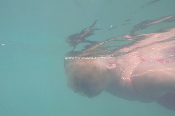 A photo of a short-haired older-woman swimming with white text overlaid "women here are raised to be mothers"