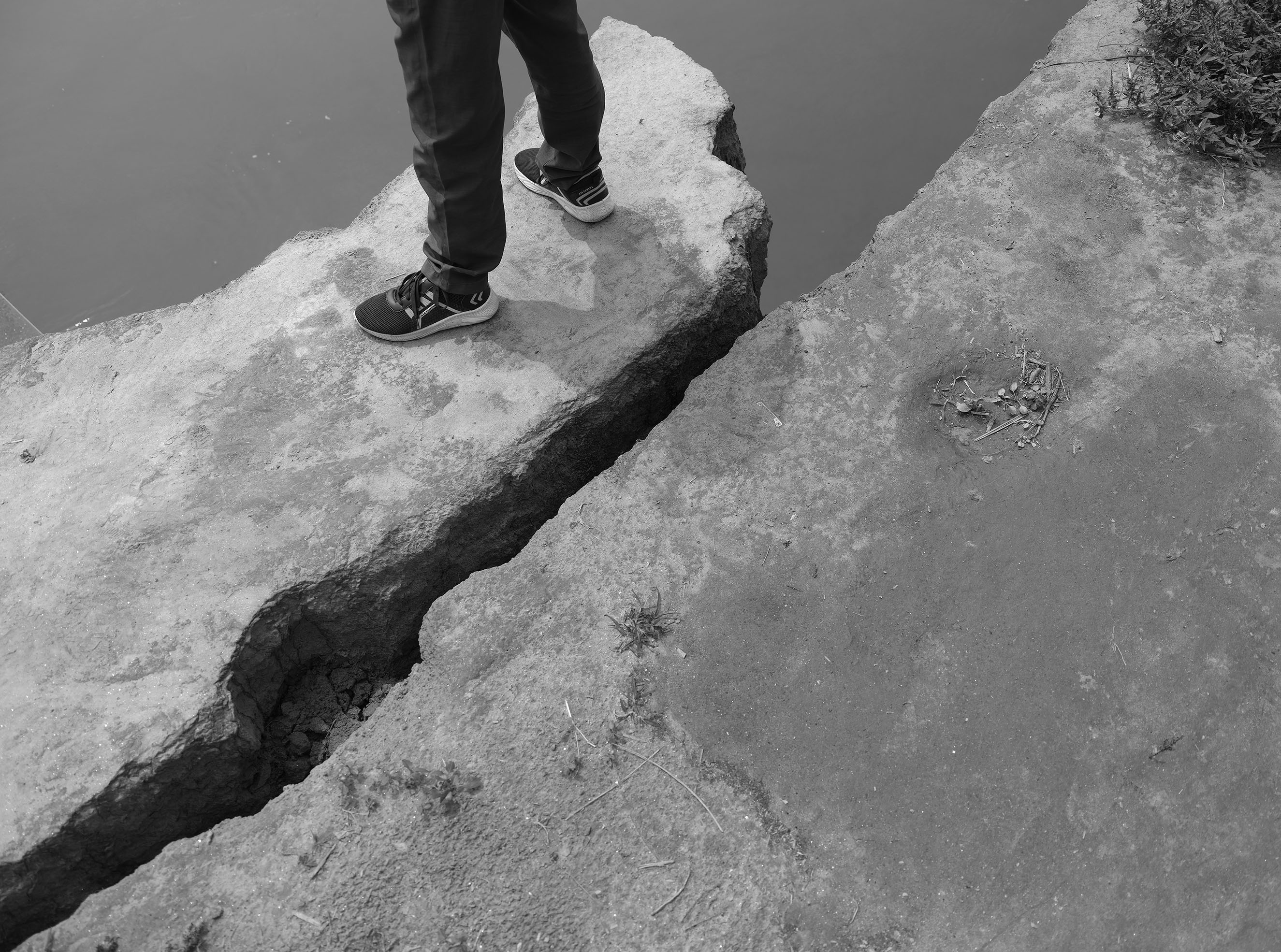 A figure stands on a cliff’s edge. The ground is split in two and only below their knees is visible.