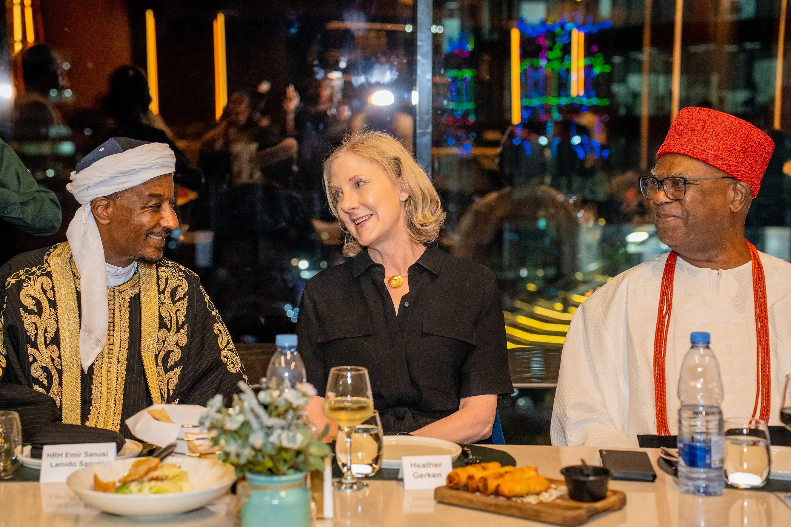 Heather Gerken sits at a formal dinner table between HRH Emir Sanusi Lamido Sanusi and another prominent Nigerian leader in traditional attire. This image highlights high-level diplomatic engagement, cross-cultural dialogue, and strategic partnership during a leadership visit to Nigeria.