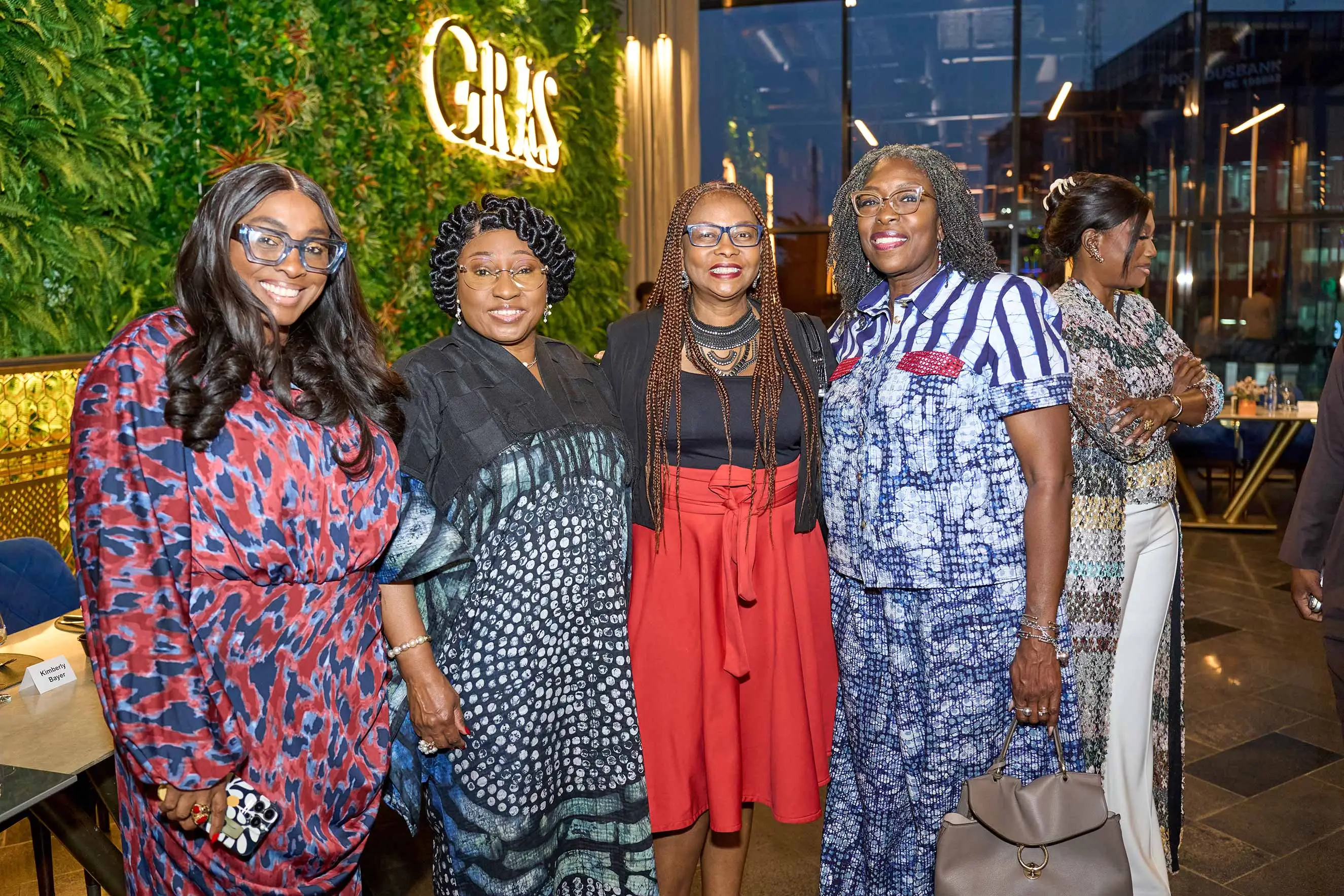 Alt Text: A diverse group of four women in stylish, patterned attire smile while posing together at an evening event. This image highlights professional networking, diverse leadership, and community building during a high-level social gathering following a strategic mission in Nigeria.