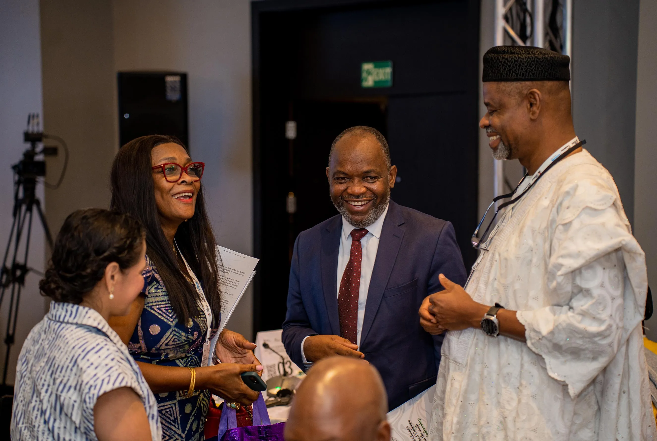 A group of four professionals in diverse business and traditional attire engage in a friendly, smiling conversation at the African Traditional and Community Leaders GBV Conference. This image captures professional networking and collaborative leadership during a strategic summit in Nigeria.