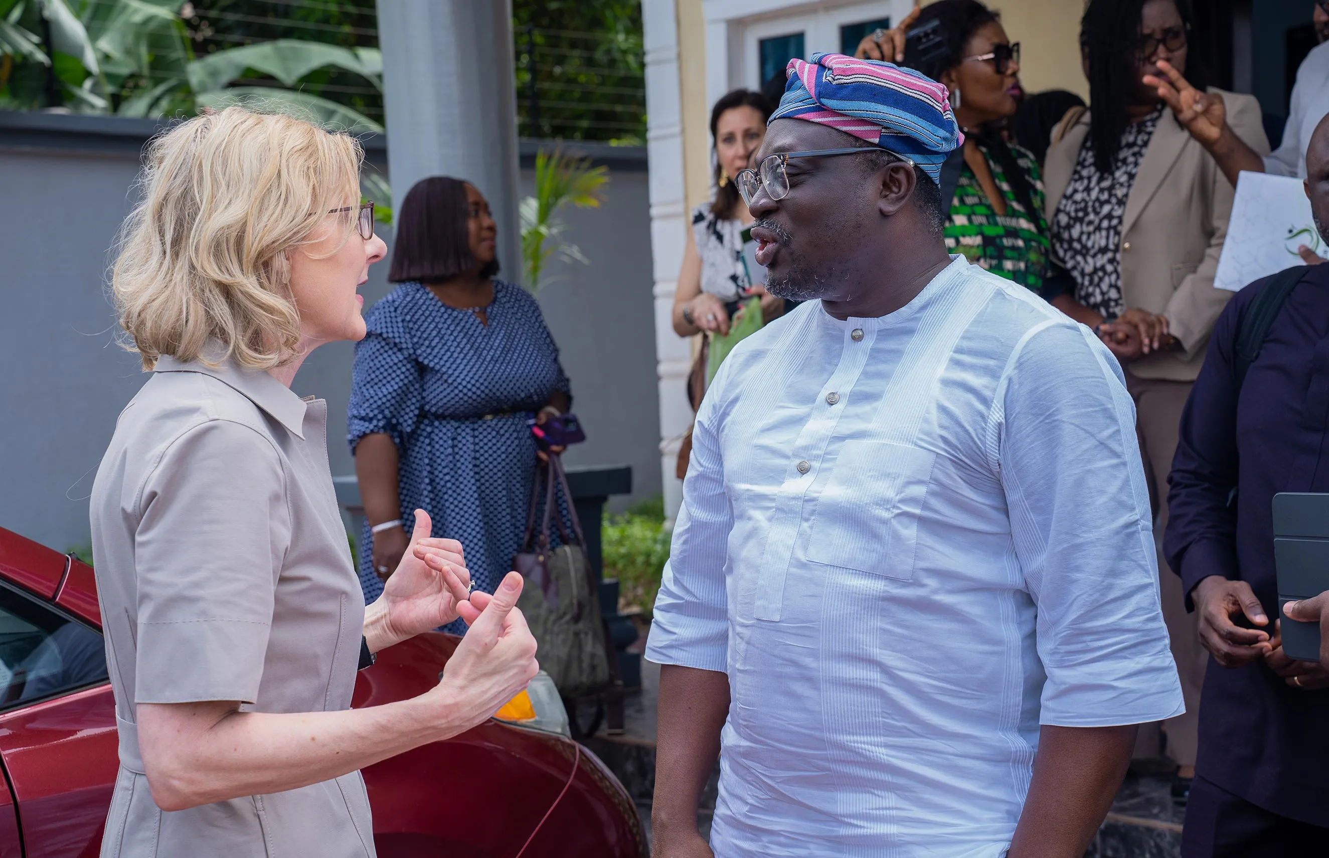Heather Gerken engages in an animated outdoor conversation with a local leader wearing a traditional blue and pink striped cap in Nigeria. This candid moment captures collaborative dialogue, local partnership, and international leadership during a strategic visit to West Africa.
