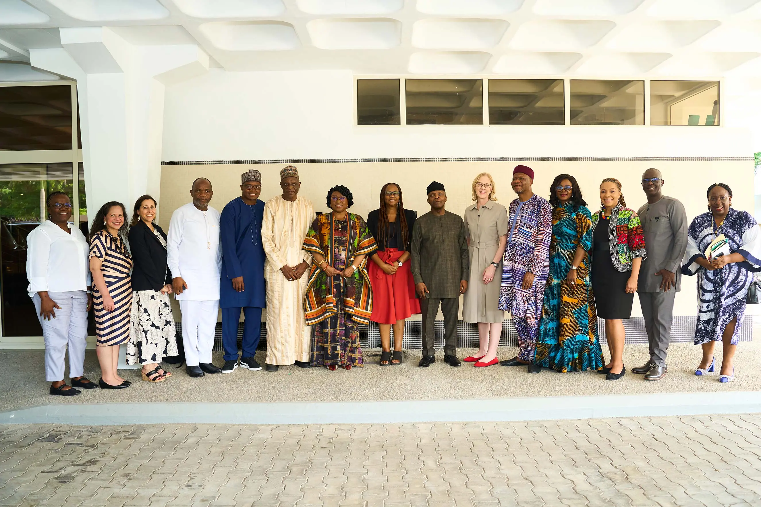 Heather Gerken and a diverse group of 14 professional and community leaders pose for a group photo outside a modern building in Nigeria. This image highlights collaborative leadership, international partnerships, and social impact during a strategic mission to West Africa.
