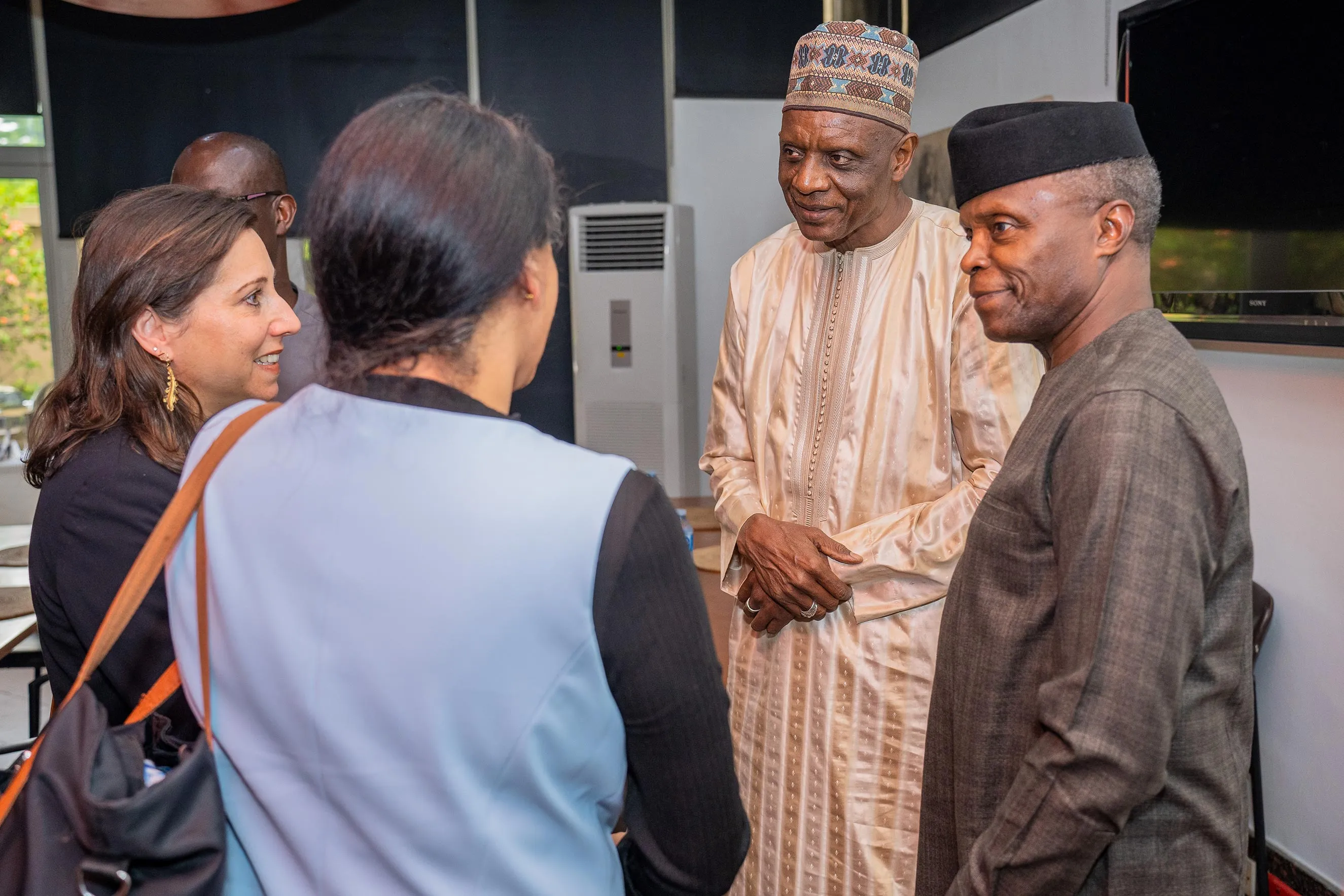A group of four professionals, including international representatives and Nigerian leaders, engage in a friendly, focused discussion indoors. This image highlights collaborative networking, diplomatic engagement, and the power of local leadership during a professional field visit to Nigeria.