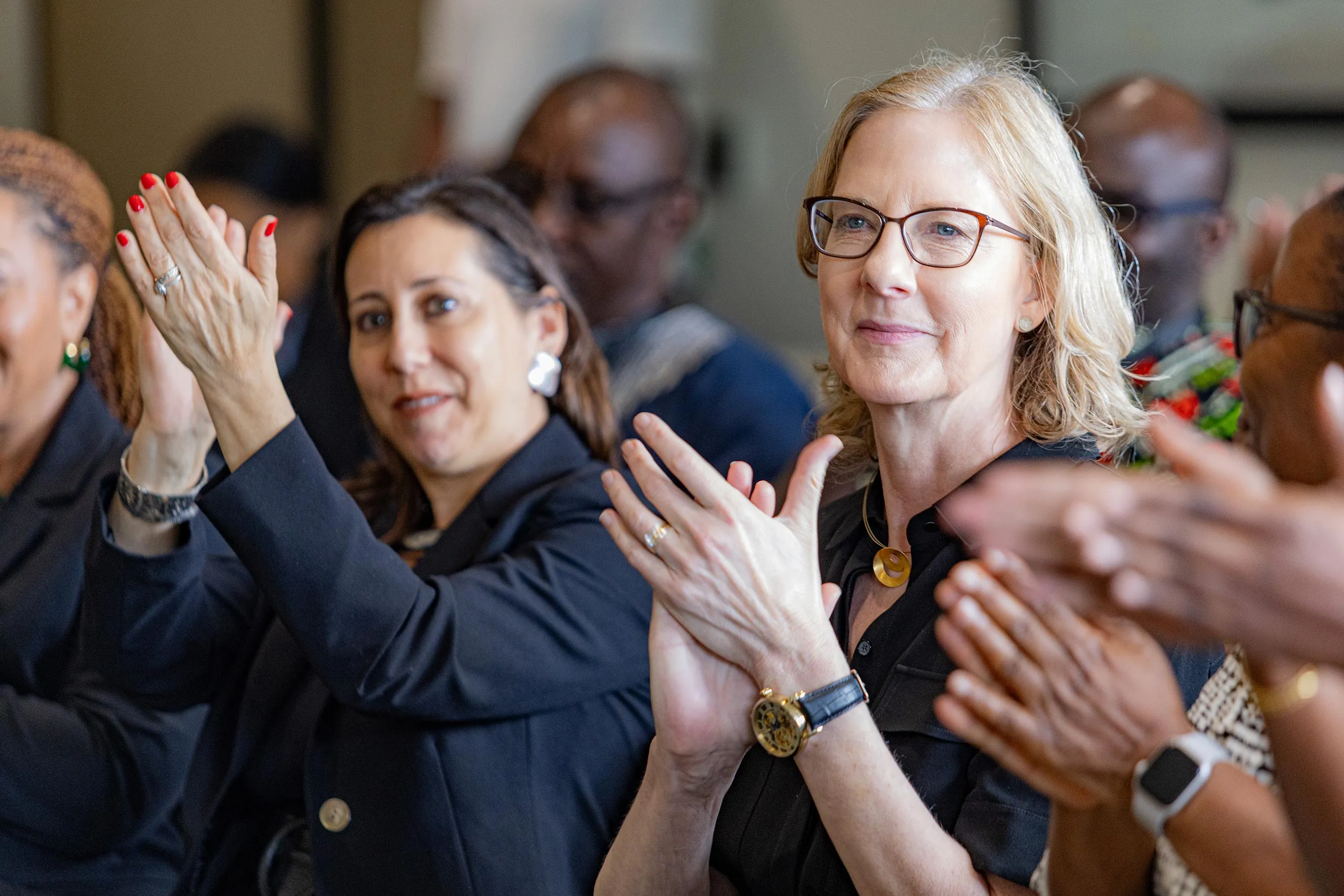 Close-up of a blonde woman with glasses in a black blouse clapping during an event. This image captures professional networking and engagement during a leadership visit to Nairobi, highlighting collaborative atmosphere and community support in an international business setting.