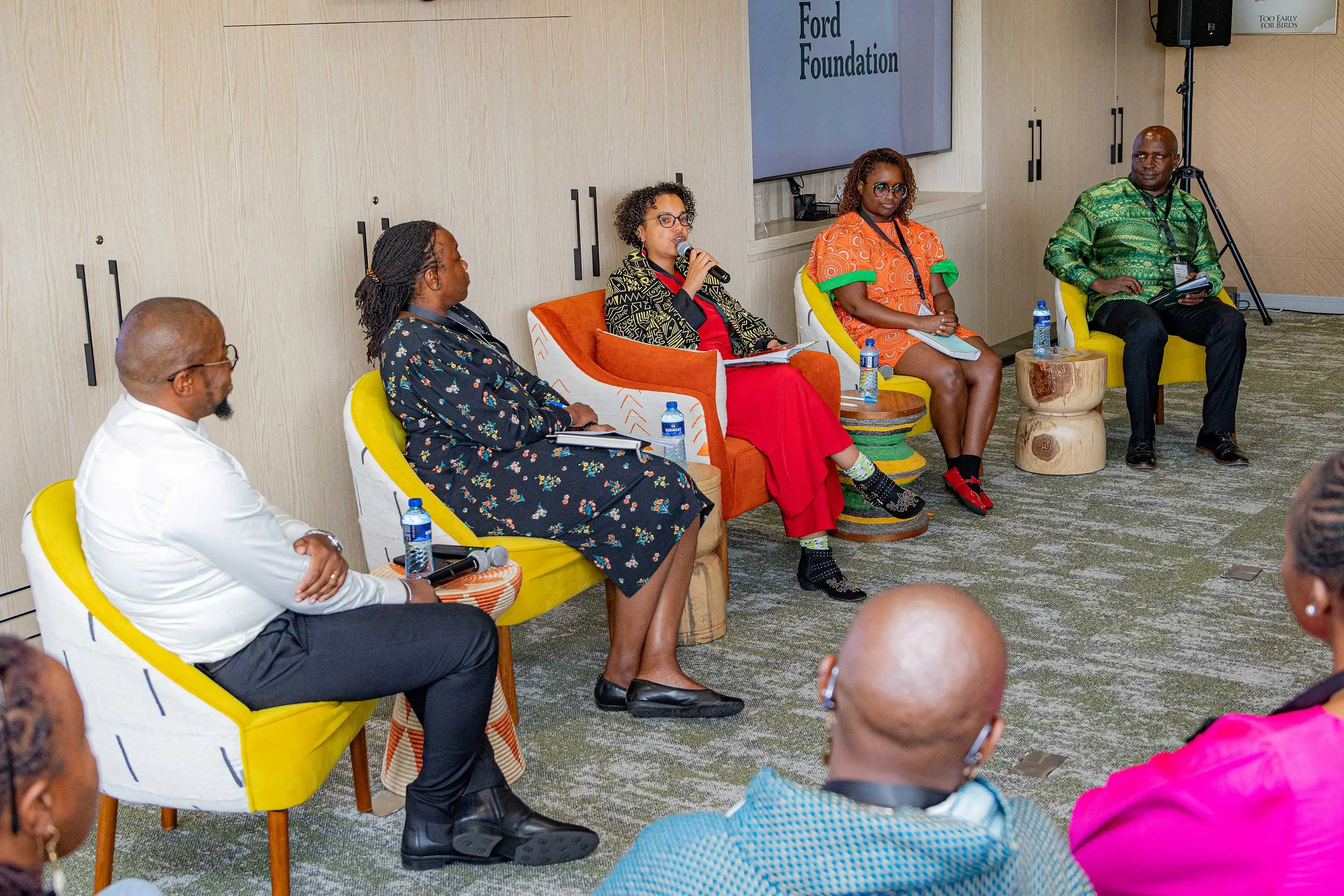 Five professionals, including four women in business attire, participate in a panel discussion at the Ford Foundation in Nairobi. Seated in modern, colorful armchairs, they engage in a strategic dialogue about international development, philanthropy, and community leadership.