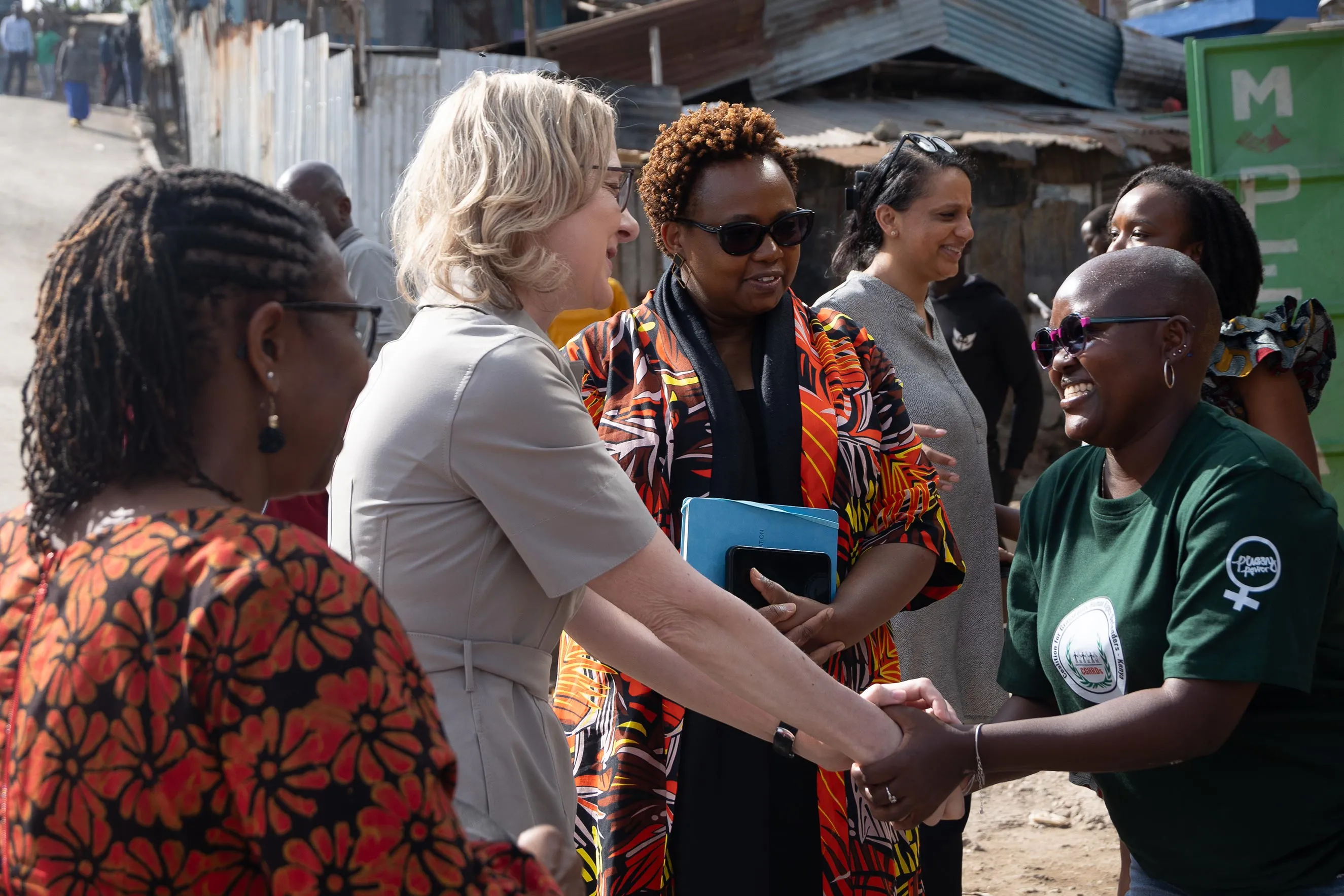 A group of women, including international leaders and local community members, engage in a warm greeting outdoors. This candid moment highlights grassroots community engagement, global philanthropy, and social impact during a professional field visit to Nairobi, Kenya.