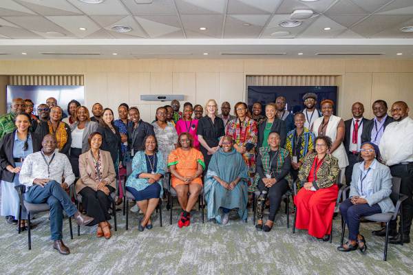 A group of approximately 30 diverse professionals pose for a group photo in a modern conference room in Nairobi. The participants are dressed in business and traditional attire, representing international development, global leadership, and collaborative networking in an office setting.