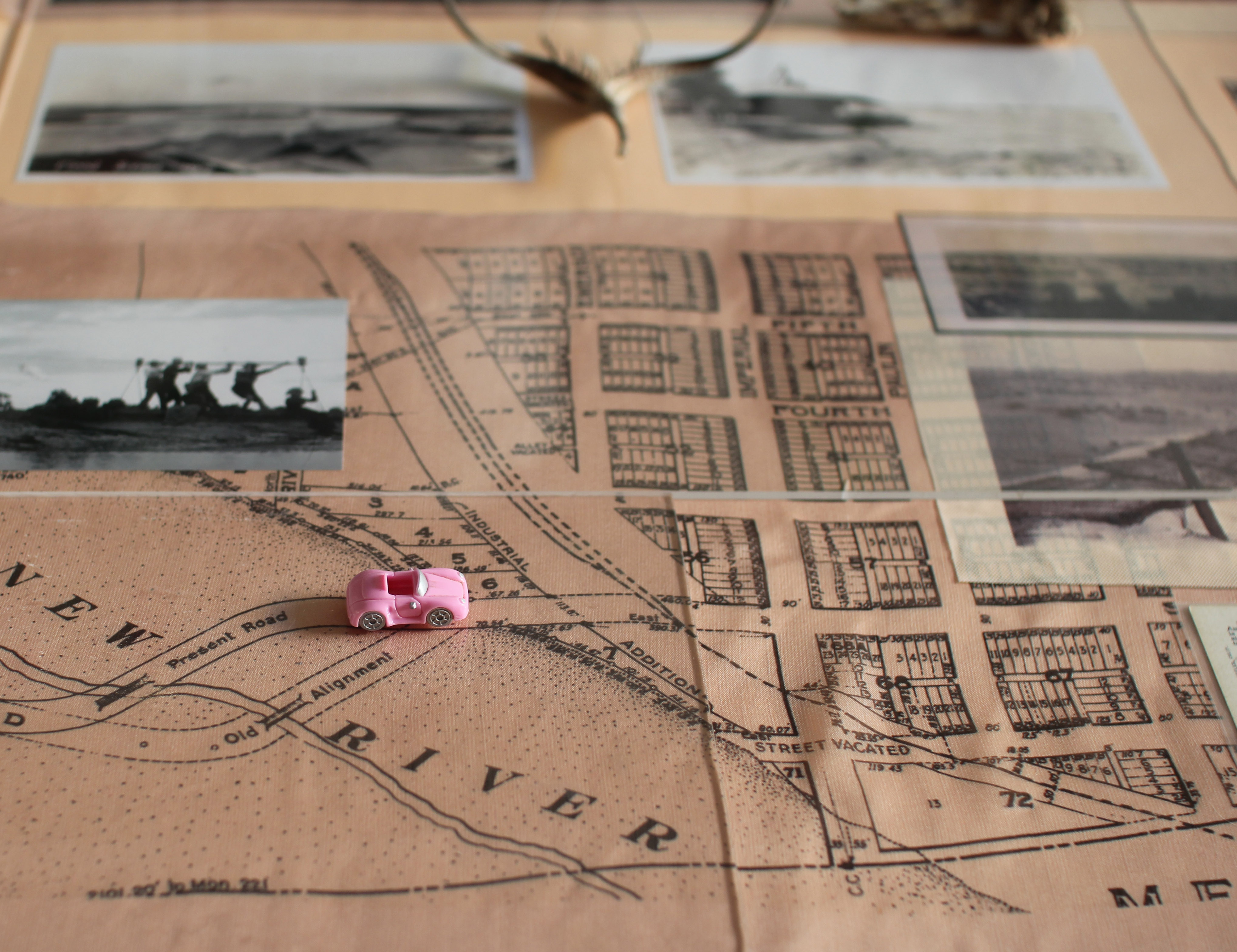 A tiny pink toy-car on top of historical maps, collaged with archival photos of people working on a river.