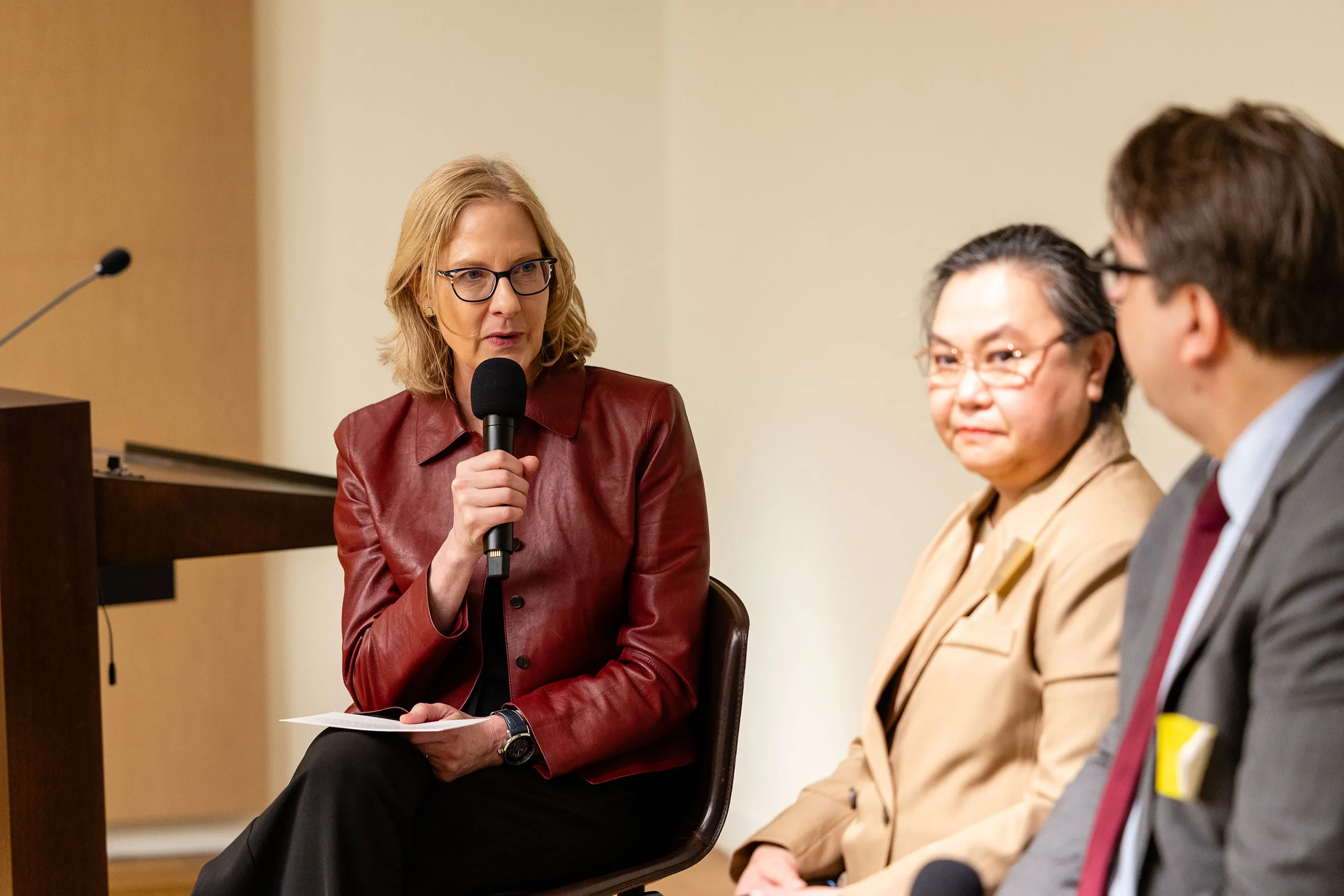 Heather Gerken speaks into a microphone while participating on a panel. Seated with other professionals, this close-up image captures a moment of leadership discussion, professional insight, and engaging dialogue during a strategic event focused on global impact and collaboration.