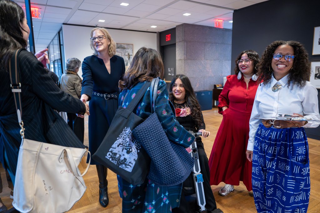 Heather Gerken smiles while shaking hands with a woman at a professional gathering. This image showcases diverse leadership, networking, and gender justice advocacy during a high-level event focused on global equity and the imperative for systemic social change.