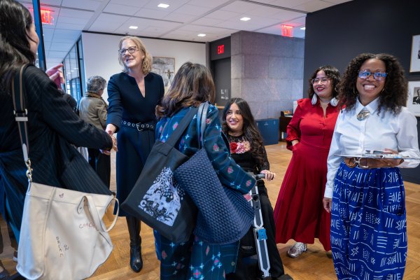 Heather Gerken smiles while shaking hands with a woman at a professional gathering. This image showcases diverse leadership, networking, and gender justice advocacy during a high-level event focused on global equity and the imperative for systemic social change.