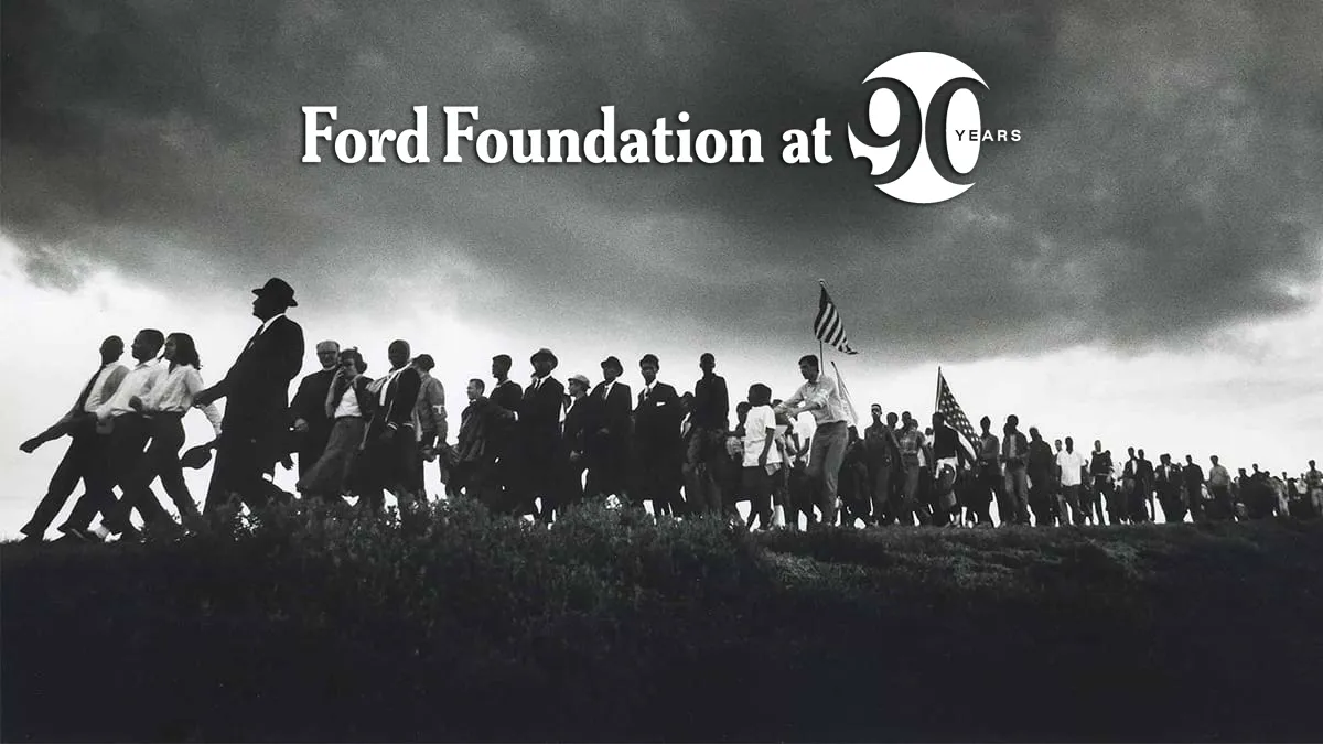 A historical photo of a crowd marching on a hill with a cloudy sky above them.