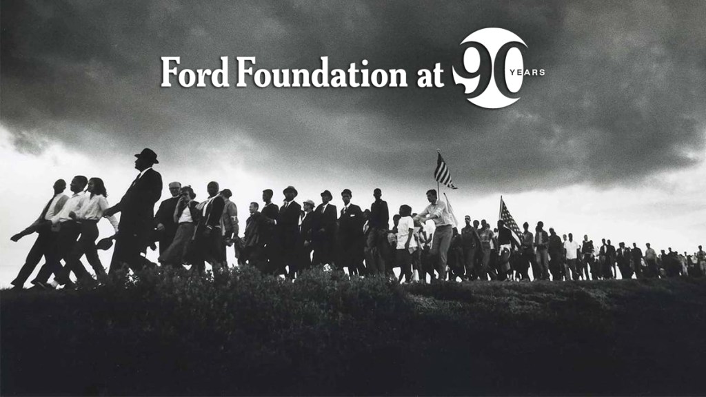 A historical photo of a crowd marching on a hill with a cloudy sky above them.