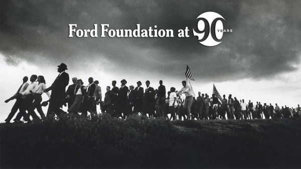 A historical photo of a crowd marching on a hill with a cloudy sky above them.