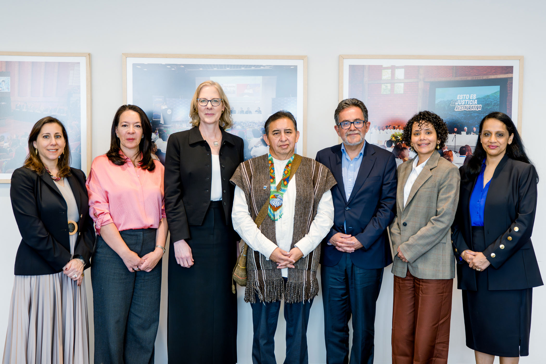 Posing in front of framed photos, Heather Gerken stands with a group of five others who wear business attire and one in traditional clothing, smiling.