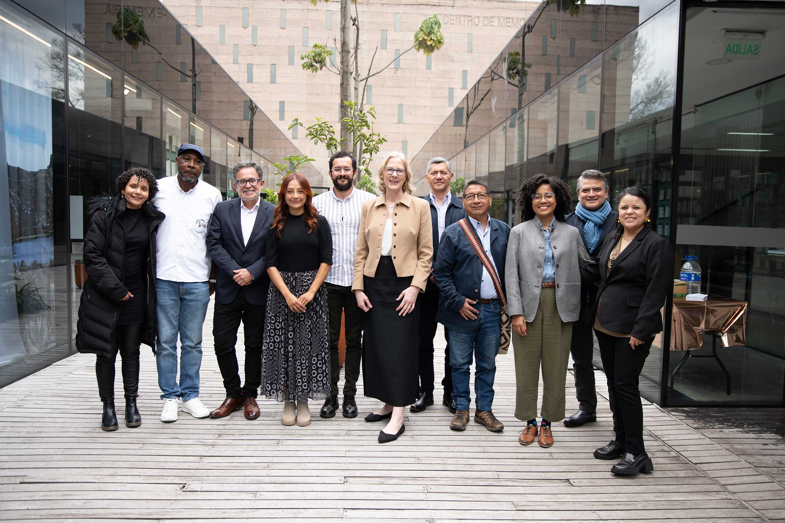 Standing in an atrium with glass walls, Heather Gerken poses with a diverse group of ten other people. The atmosphere is professional and friendly, conveying unity.