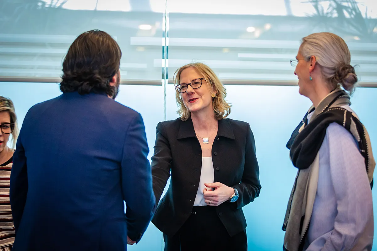 An action-oriented photo of Heather Gerken in glasses and a black blazer smiling while shaking hands with a man. This journalistic image captures a moment of professional collaboration, helping to humanize the foundation’s regional work and partnerships.