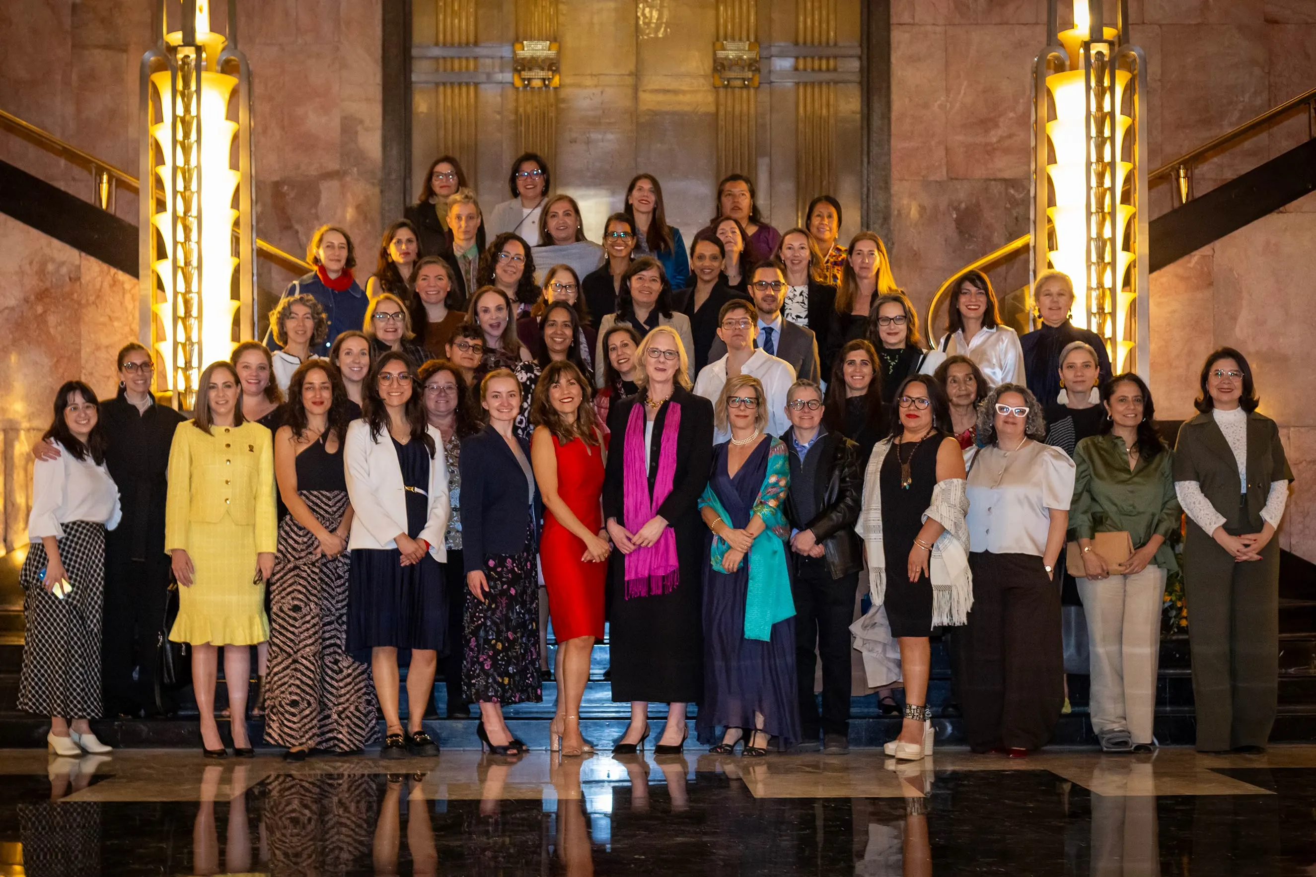 A large group of over 40 diverse professional staff members posing together for a formal portrait on a grand, marble staircase with art deco lighting. This high-quality photograph humanizes the foundation’s work by capturing a moment of collective partnership during a regional visit.