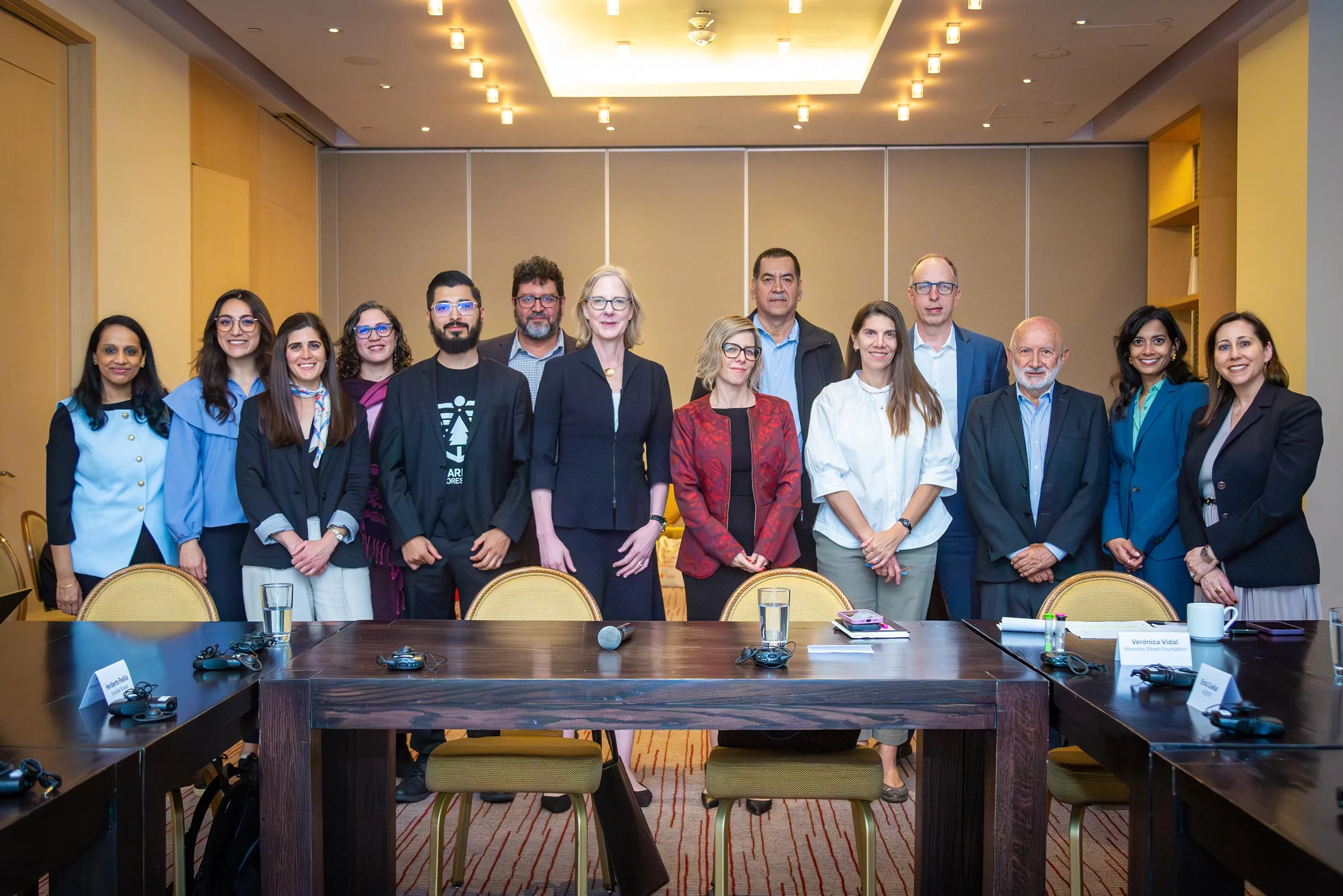 A group portrait of 14 professional staff members standing together in a formal meeting room with a large wooden conference table in the foreground. This image humanizes the foundation’s work and highlights collaborative efforts during a regional office visit.