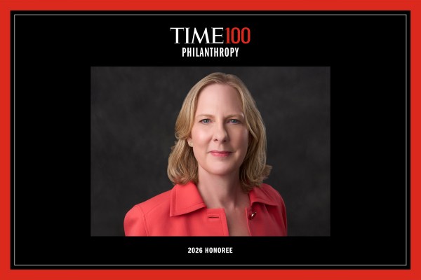 A smiling woman, Heather Gerken, with blonde hair, wearing a bright coral blazer. The image is framed by a black-and-red border with text reading "TIME100 PHILANTHROPY 2026 HONOREE." This high-quality photo humanizes our leadership and highlights institutional recognition.