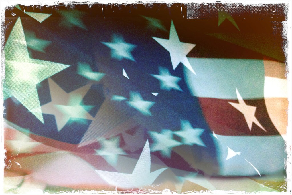 An abstract, stylized graphic of a waving American flag with layered, floating white stars and translucent red and blue stripes. The image features a distressed, vintage-style white border, representing themes of democracy and American patriotism.