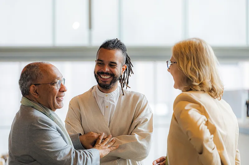 Heather stands together with two other people, smiling and talking in a brightly lit room.