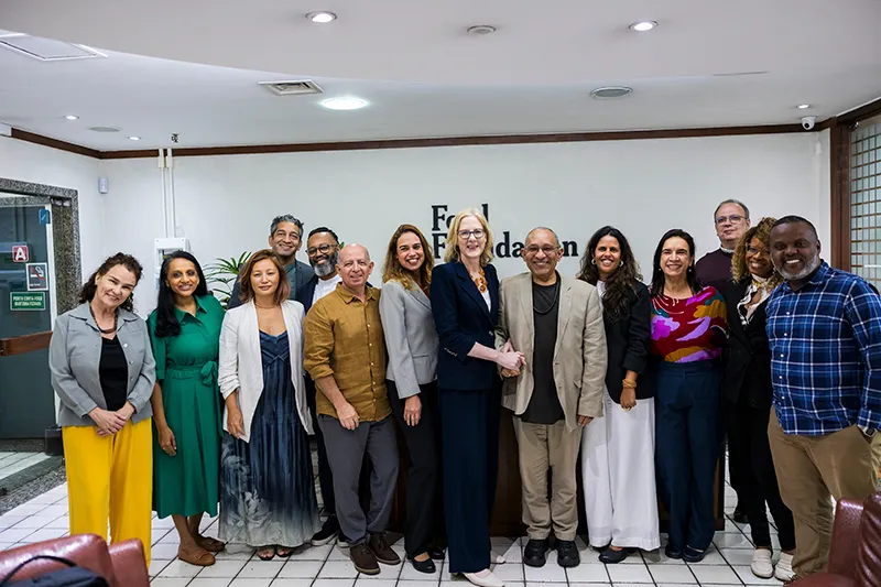 Staff pose for a group photo with Heather and Átila in the front and center. Individuals are pictured with big smiles in front of a sign that says “Ford Foundation,” wearing a variety of professional-looking, colorful outfits.