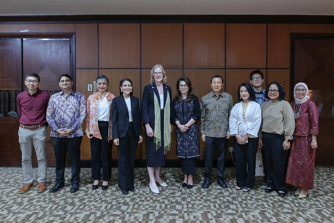 Ten professional leaders standing together in front of a dark wood-paneled wall. This journalistic photograph humanizes our global team, capturing a moment of institutional collaboration during a regional office visit to Jakarta, Indonesia.