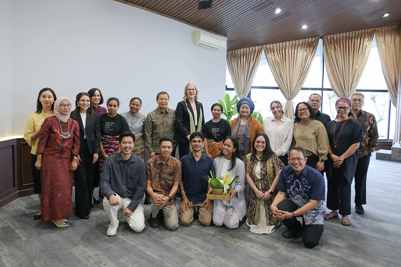 Group portrait of over 15 professional staff members and regional partners posing together in a bright, modern room. This journalistic photograph captures a moment of global partnership and collaboration during an institutional visit to Jakarta, Indonesia.