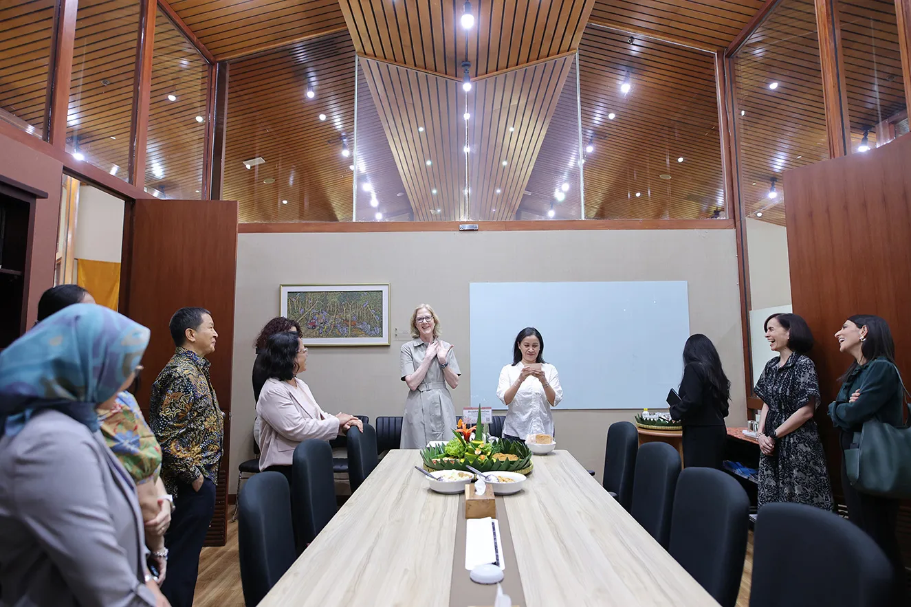 A group of professional staff members gathers around a long wooden conference table under a vaulted wooden ceiling in the Jakarta office. This high-quality photograph captures an engaging, collaborative moment, humanizing our global team and work.
