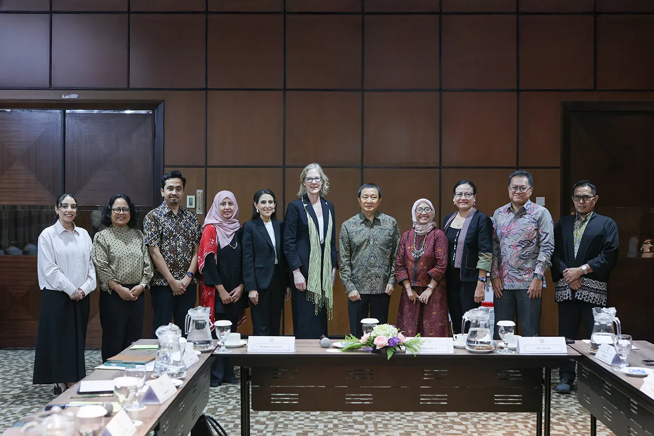 A high-quality group portrait of 11 professional staff members standing together behind a conference table in Jakarta, Indonesia. This journalistic photograph captures a moment of regional office collaboration , humanizing the foundation's global team and its institutional work.