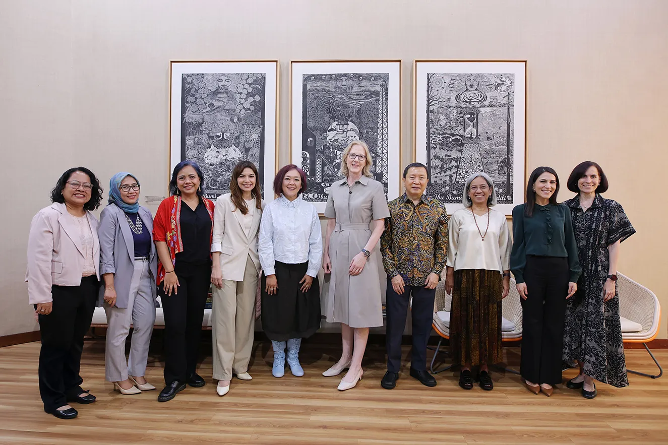 A high-quality group portrait of ten professional staff members standing together in front of three large, framed black-and-white art prints. This journalistic photograph humanizes the global team, capturing a moment of regional office collaboration during a visit to Jakarta, Indonesia.