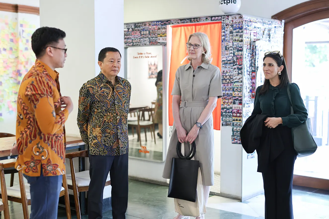 Professional leaders standing in an office lobby, listening to a colleague speak. This action-oriented, journalistic photograph captures an engaging, collaborative moment, humanizing our global team and work during a regional office visit to Jakarta, Indonesia.