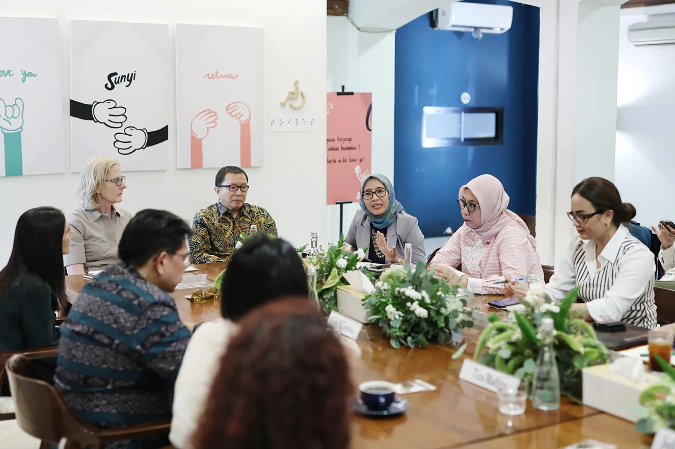 Professional leaders engaged in a collaborative meeting around a wooden conference table. A woman in a grey hijab speaks while others listen closely. This action-oriented, journalistic photograph humanizes our global team during a regional office visit to Jakarta, Indonesia.