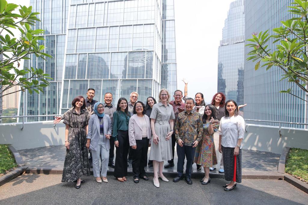 A high-quality group portrait of 14 professional staff members posing together on an outdoor terrace in Jakarta. Towering glass skyscrapers stand in the background. This image humanizes the foundation's global team and highlights collaborative engagement during a regional office visit.