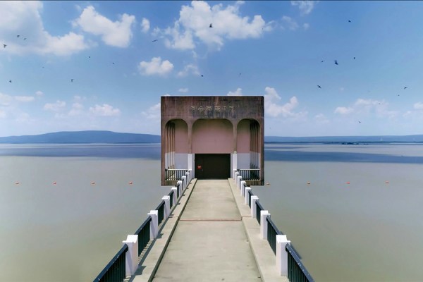 A concrete railed walkway leading to the Sardis Dam outlet structure at Sardis Lake, Mississippi, with blue sky and clear water in the background.